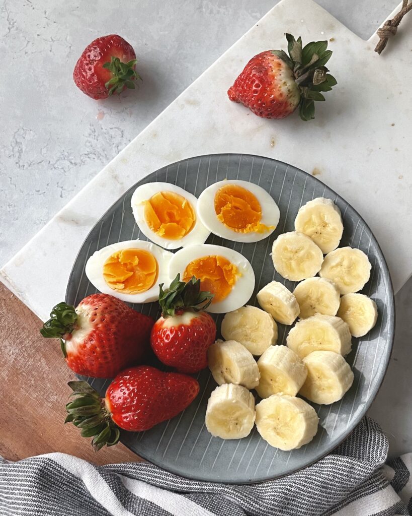 Kokt ägg med jordgubbar och banan på tallrik – enkel frukost med protein för kvinnor 40+